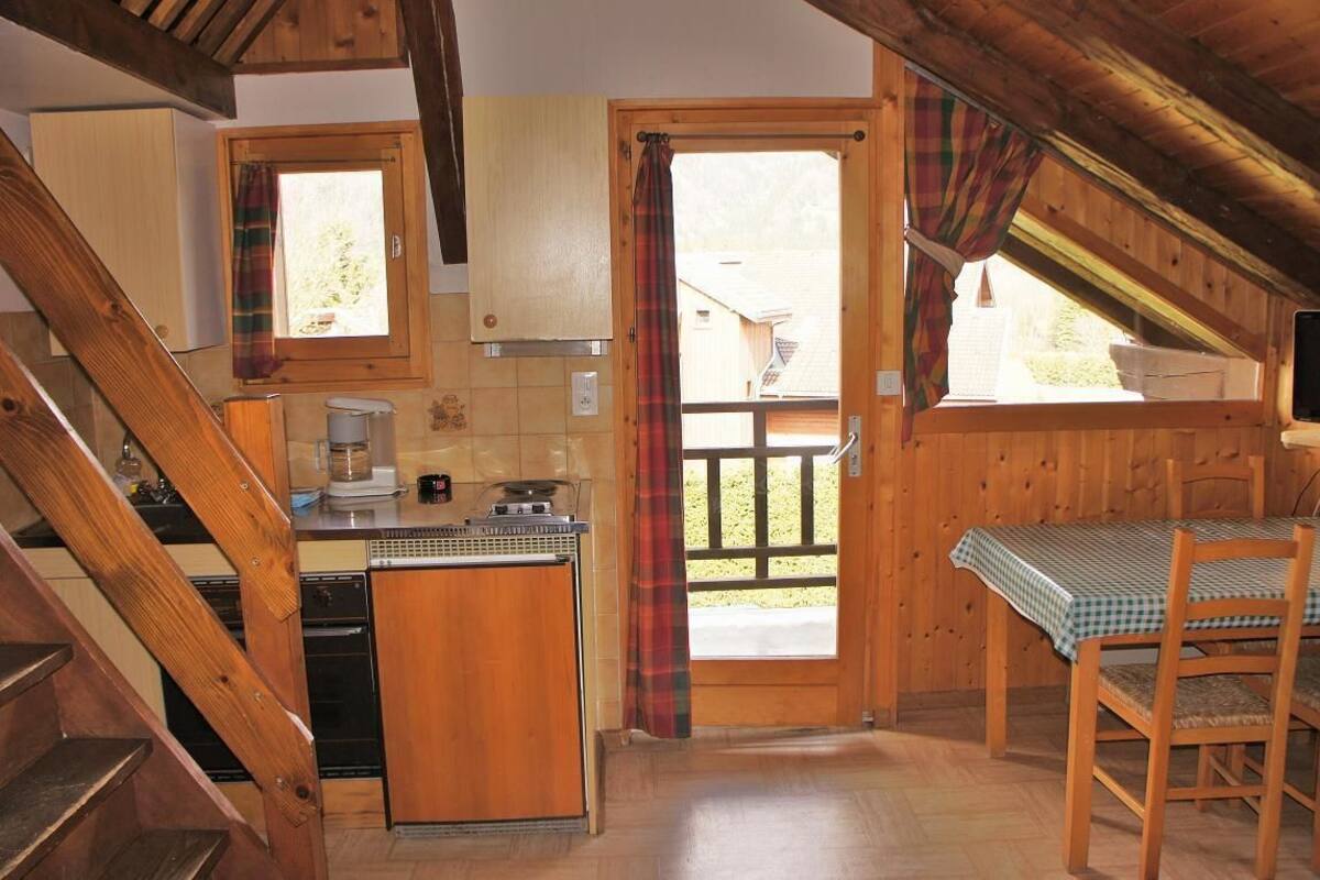 A kitchen with wooden cabinets, a stove, and a window with a plaid curtain.