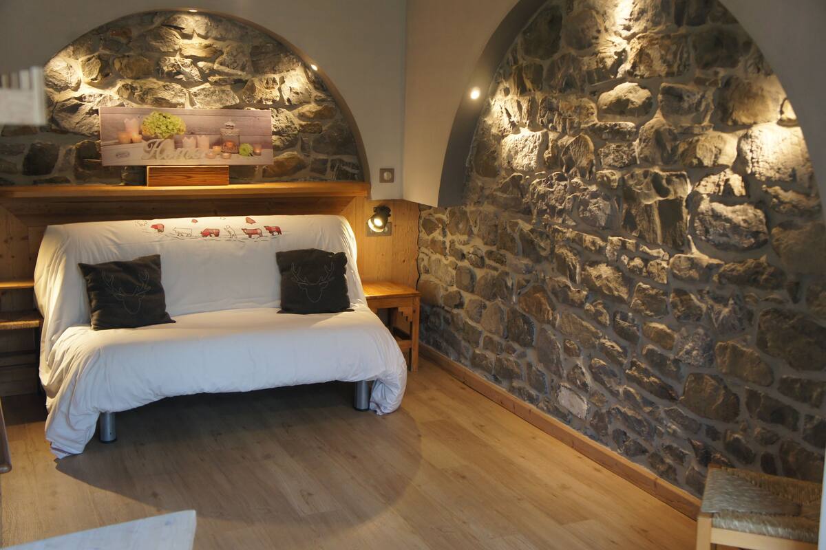 A cozy room with a stone wall, a wooden bench, and a bed with white bedding and two pillows.