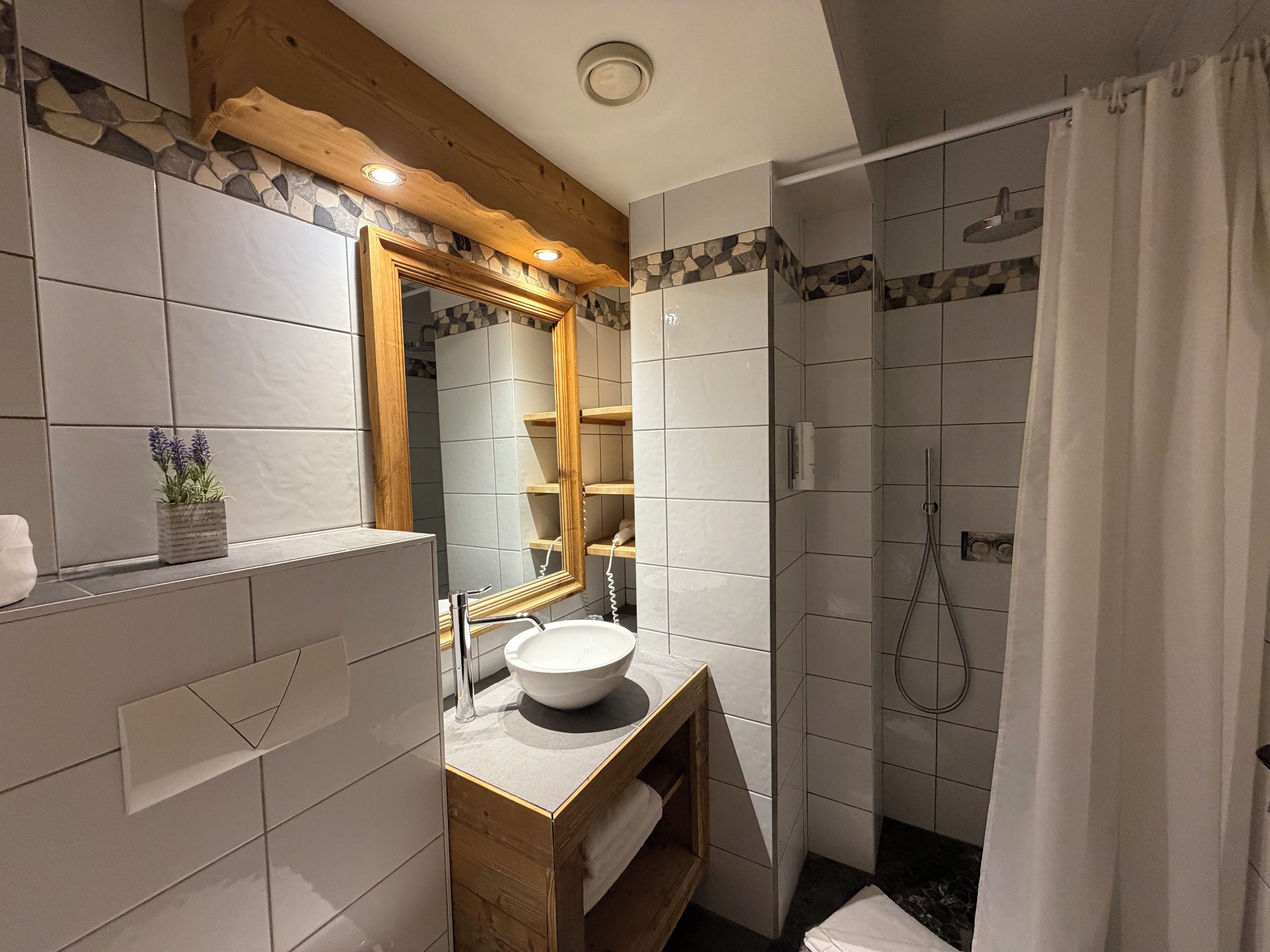 A bathroom with a wooden vanity, a large mirror, a white sink, and a shower area.
