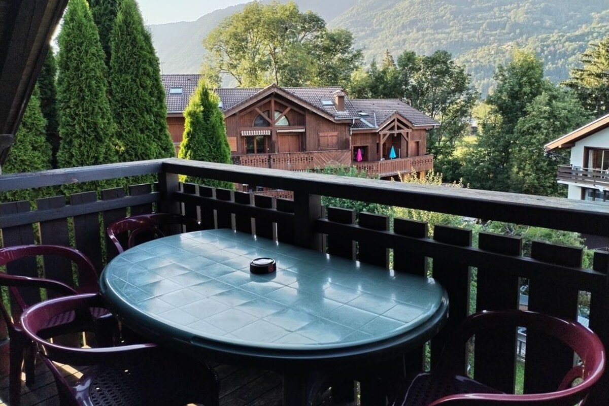 A balcony with a round table and chairs, overlooking a mountainous landscape with houses.