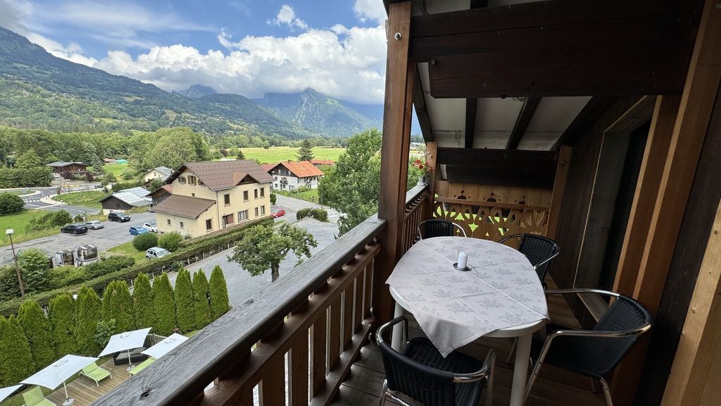 A balcony with a table and chairs, overlooking a village and mountains.