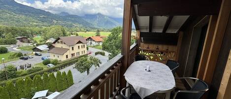 A balcony with a table and chairs, overlooking a village and mountains.