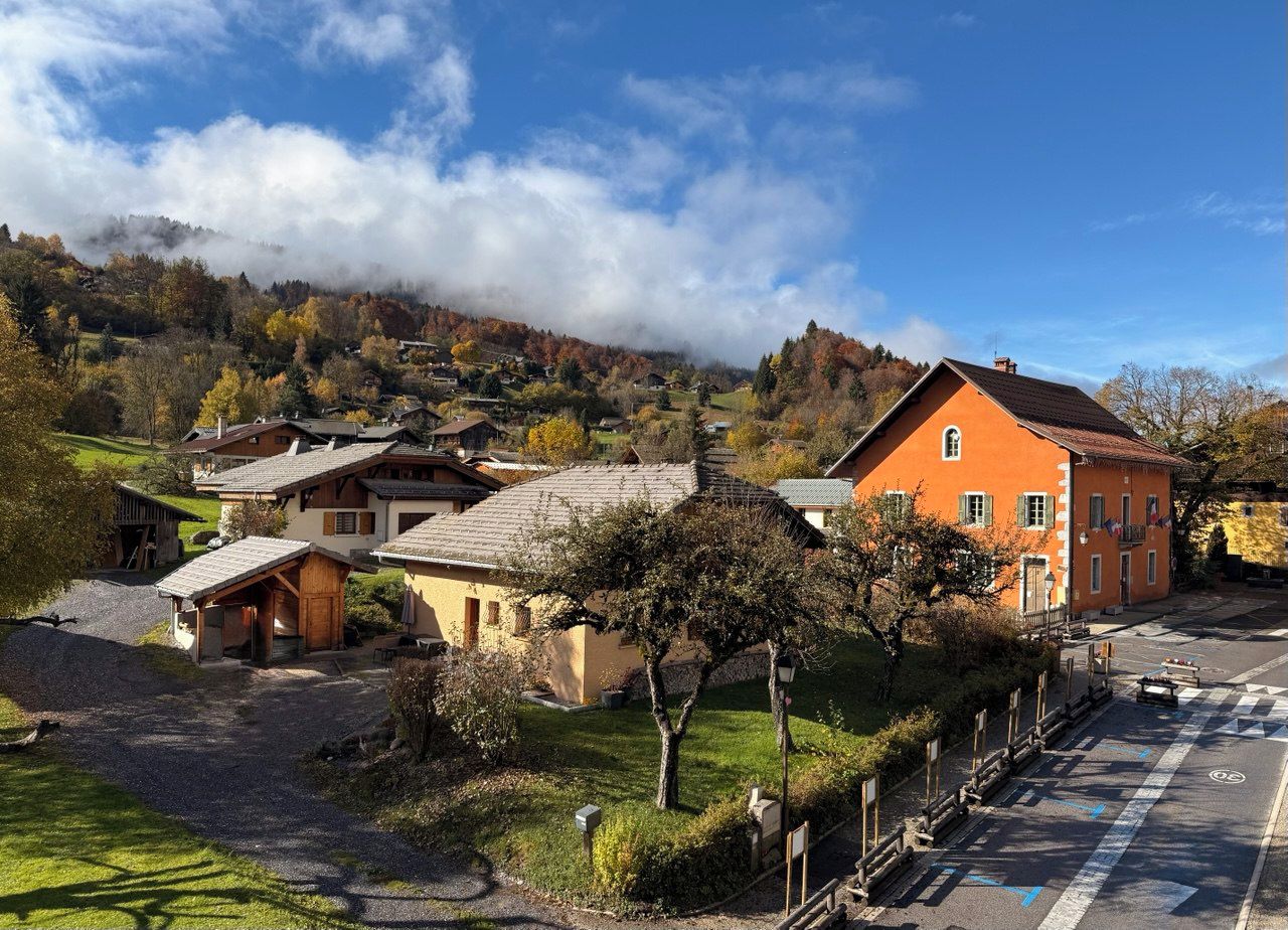 A village with traditional houses, a main building with a red facade, and a road with a speed limit sign.