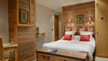 Un dormitorio con paneles de madera, una cama con ropa de cama roja y blanca, una mesita de noche con una lámpara y un aparador de madera.