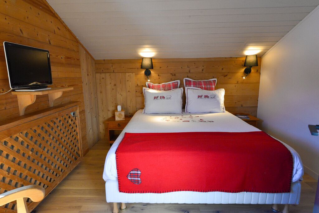 A wooden-paneled room with a bed, a TV, and two wall-mounted lamps.