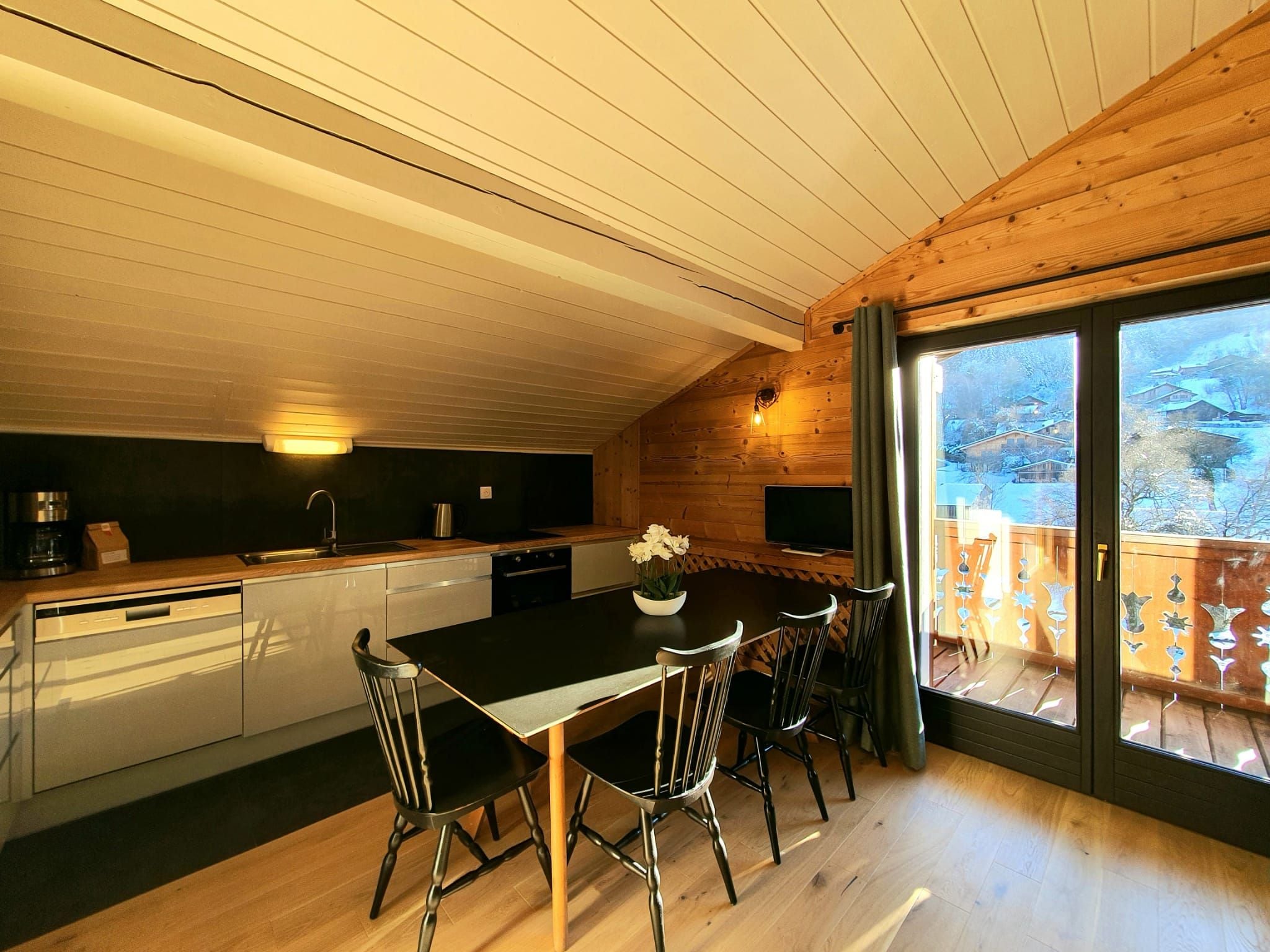A modern kitchen with a central island, wooden ceiling, and a view of a snowy landscape through large windows.
