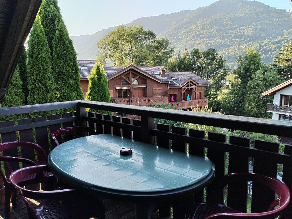 A balcony with a round table and chairs, overlooking a mountainous landscape with houses.