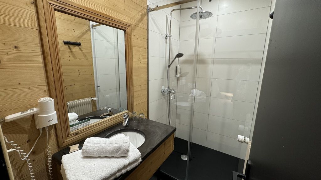 A bathroom with a wooden vanity, a mirror, a sink, a towel, and a glass-enclosed shower.