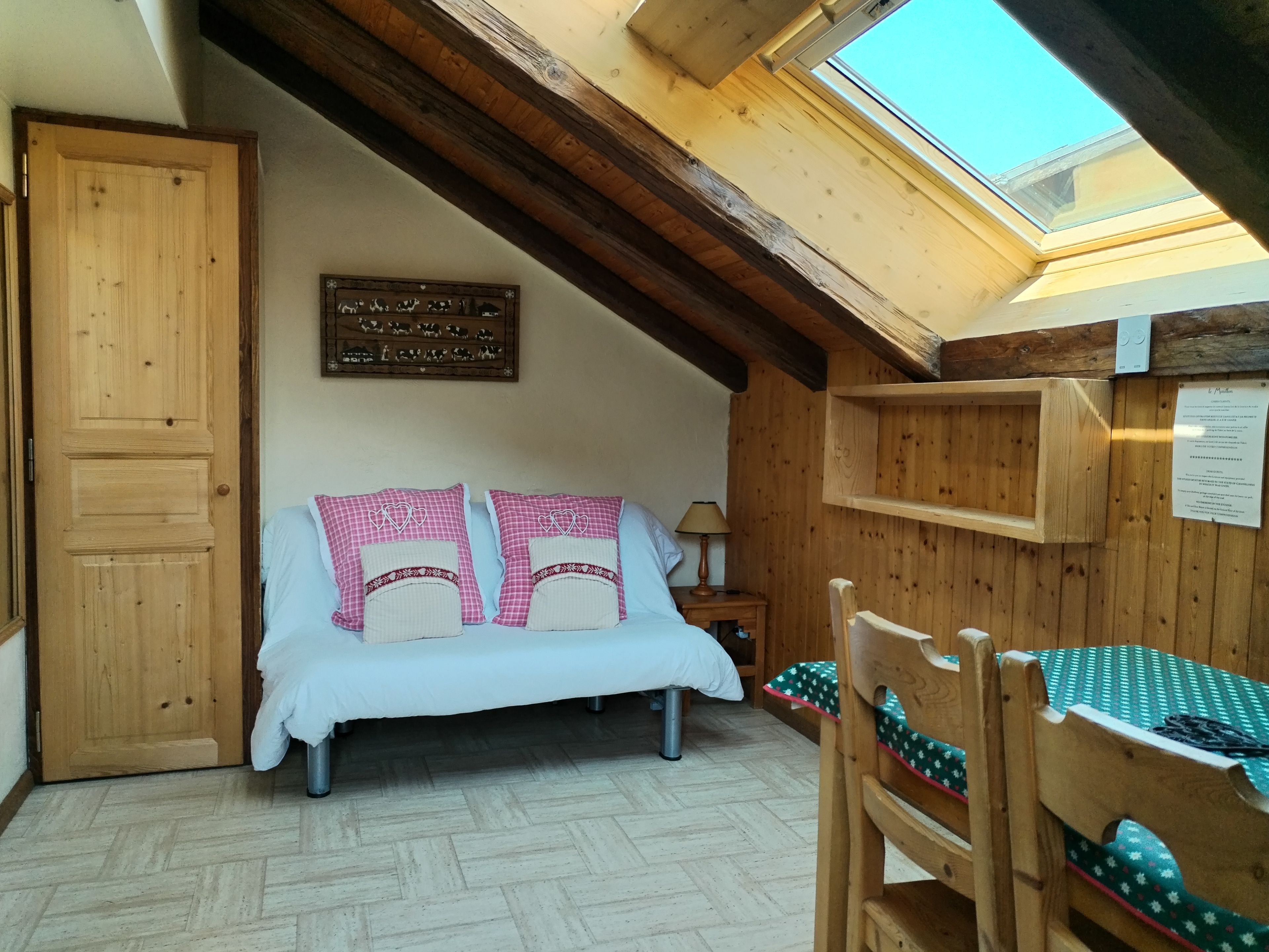 A cozy bedroom with a bed, wooden walls, a skylight, and a wooden door.