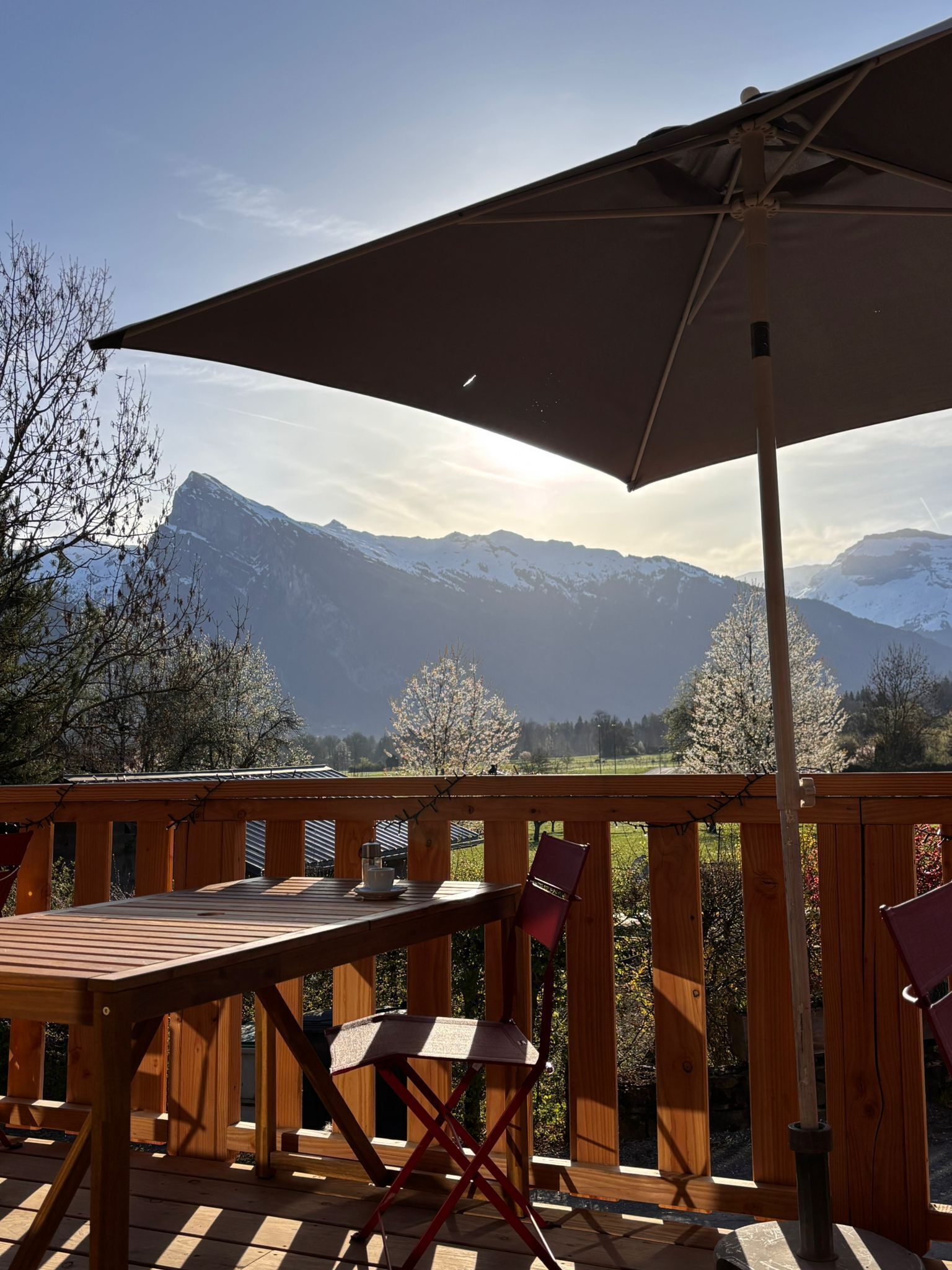 Una terraza de madera con una mesa, sillas y una sombrilla, con vista a la montaña.