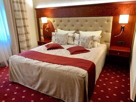 Quarto de hotel com uma cama grande, duas mesas de cabeceira e cabeceira com iluminação embutida.