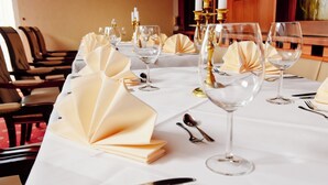 Une table dressée pour un repas formel, avec des nappes blanches, des chandeliers dorés et des serviettes pliées.