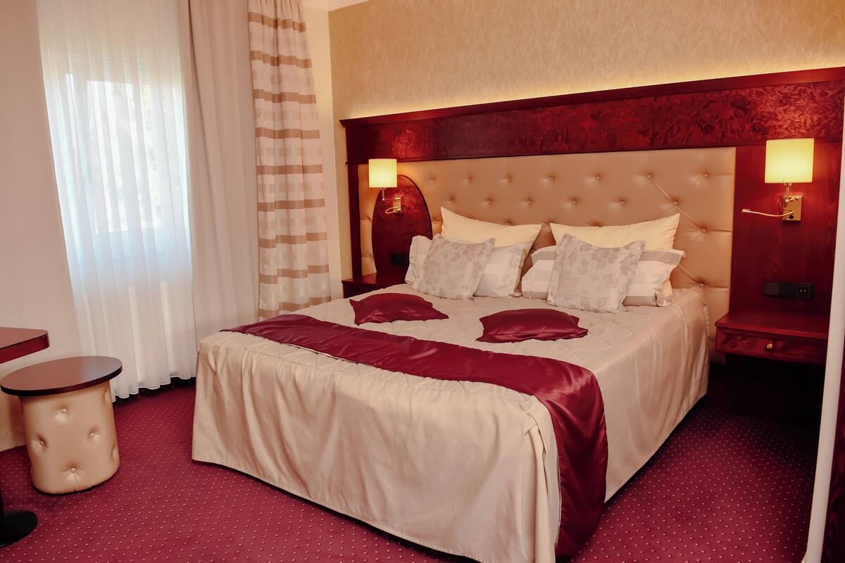 A hotel room with a large bed, a bedside table, a lamp, and a window with curtains.