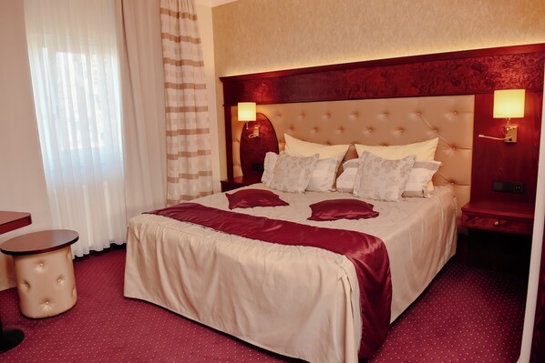 A hotel room with a large bed, a bedside table, a lamp, and a window with curtains.