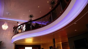 Un balcon incurvé avec des garde-corps en verre, un lustre et des plantes en pot.