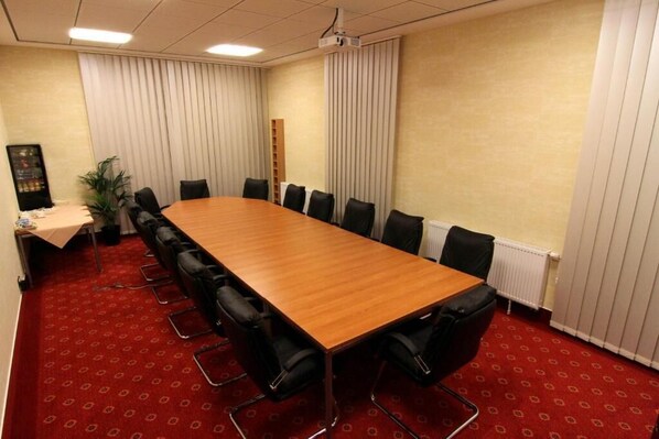 Une salle de conférence avec une longue table en bois, des chaises noires, un projecteur et un sol recouvert d’une moquette rouge.