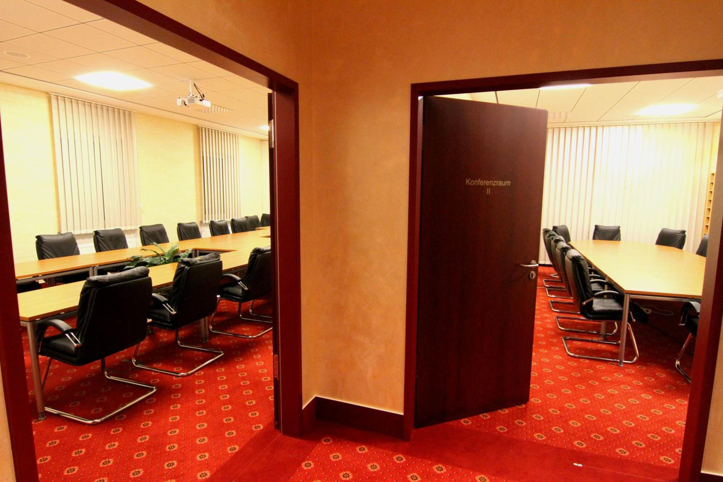 Ein Konferenzraum mit einem langen Tisch, mehreren Stühlen und einem roten Teppichboden.