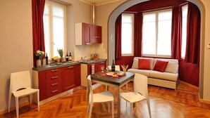 A compact living space with a kitchenette, a dining area with a table and chairs, and a sofa in a cozy corner. - VIlla Maurice (Stresa)