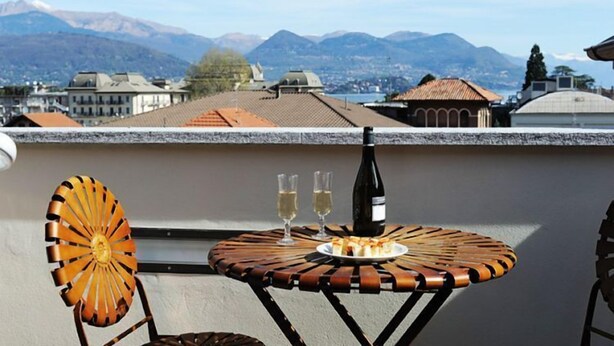 A round table with a bottle of wine, two glasses, and a plate of food on a terrace with a mountain view. - VIlla Maurice (Stresa)