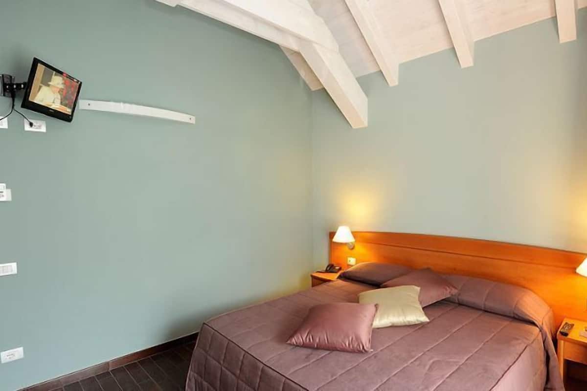 A bedroom with a bed, two bedside lamps, a nightstand, and a wall-mounted TV.
