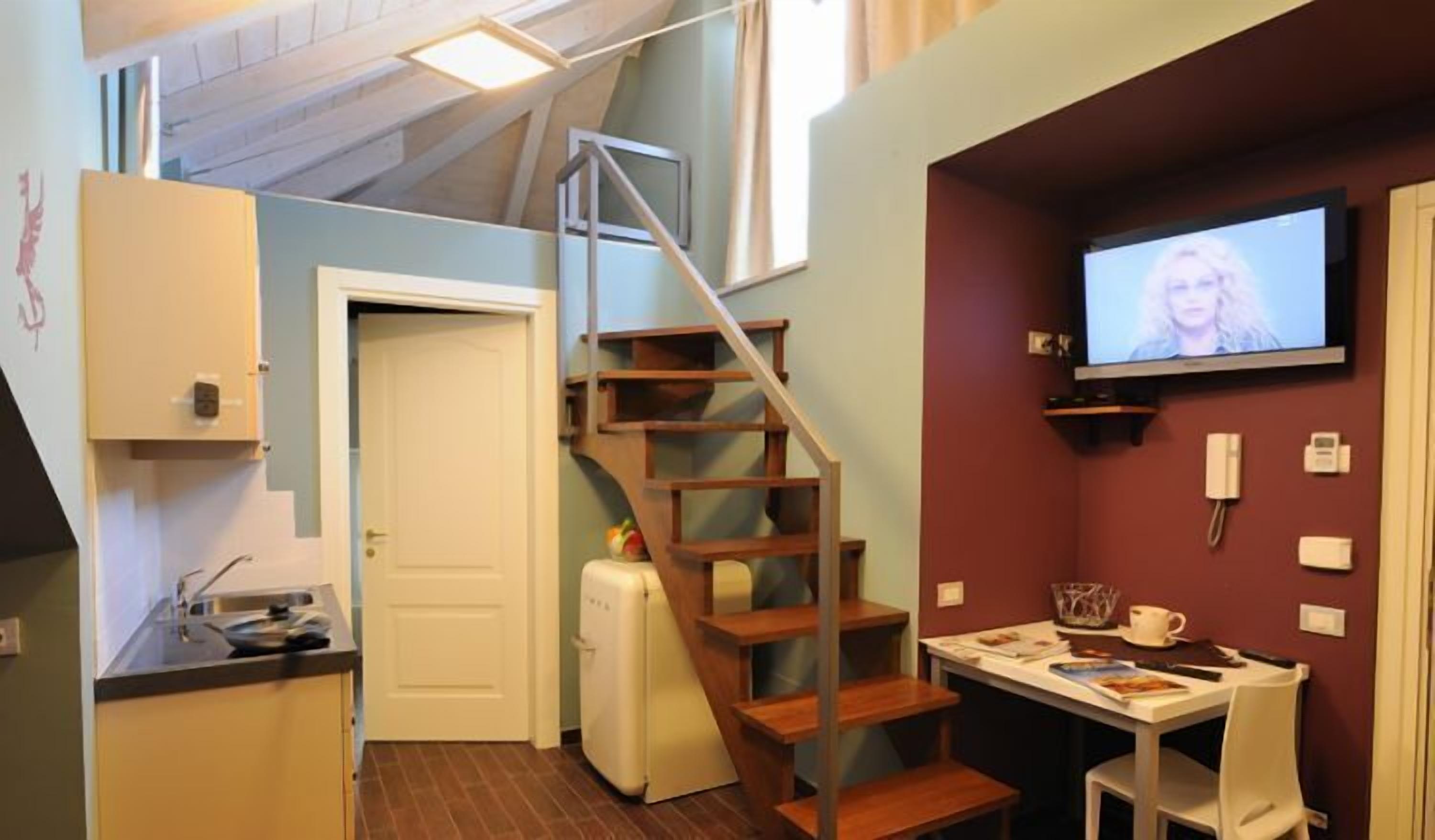 Eine kompakte Küche mit einer Holztreppe, einem Kühlschrank, einem Esstisch mit Stühlen und einem an der Wand befestigten Fernseher.