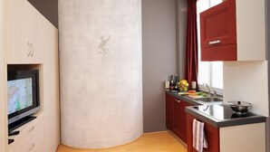 A compact kitchen with a flat-screen TV, a red cabinet, and a window with curtains. - VIlla Maurice (Stresa)