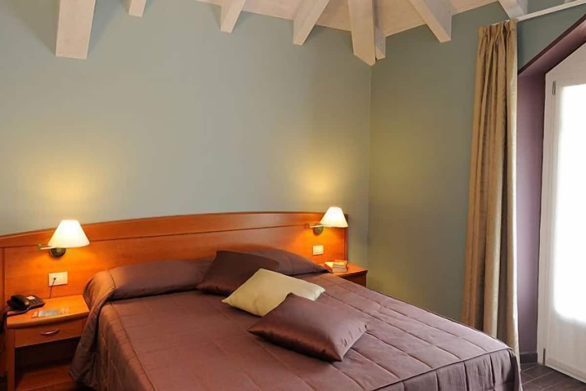 A hotel room with a large bed, two bedside lamps, a telephone, and a window with curtains.