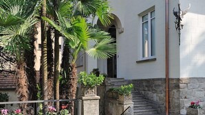A building with a stone staircase leading to a door, surrounded by palm trees and potted plants. - VIlla Maurice (Stresa)