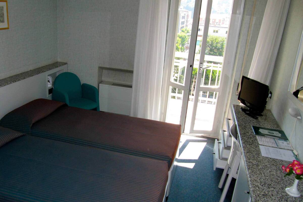 A hotel room with a bed, a desk, a chair, a television, and a window with a view of buildings.