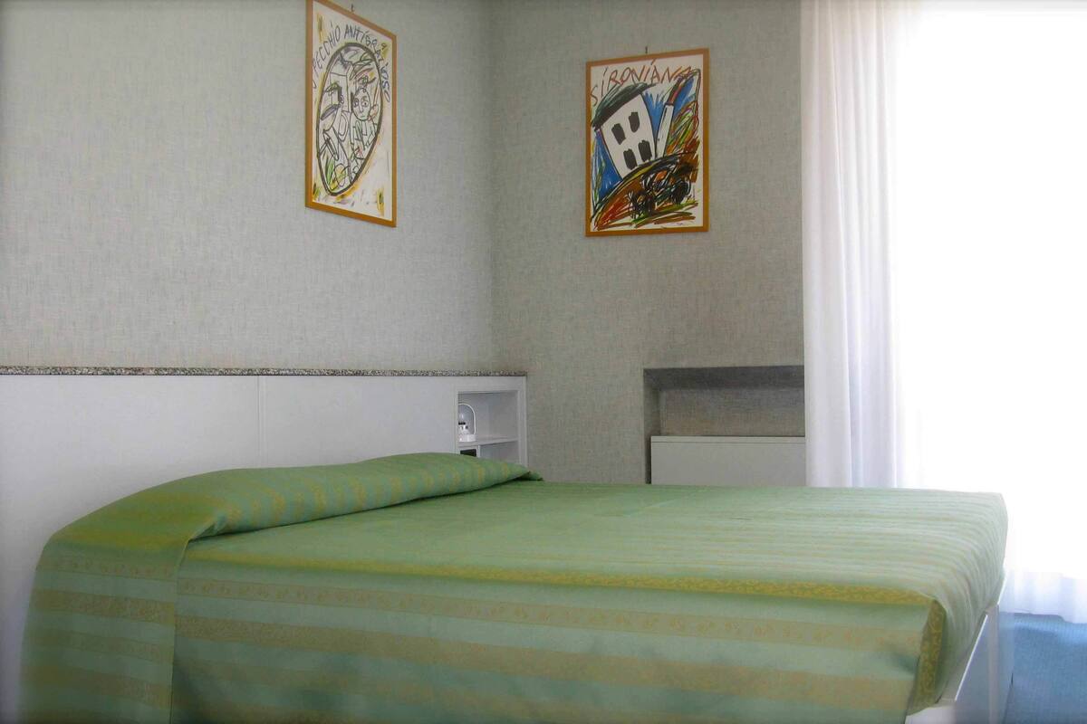 A hotel room with a bed, a nightstand, and two framed artworks on the wall.