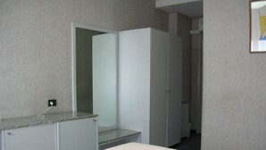 Quarto de hotel com cama, pequena escrivaninha, espelho e guarda-roupa.