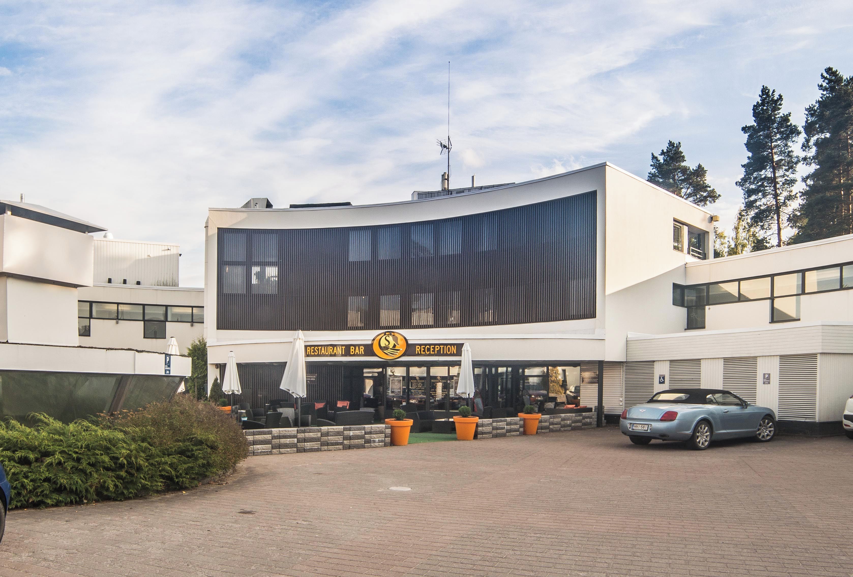 A modern building with a reception area, outdoor seating, and a parking area.