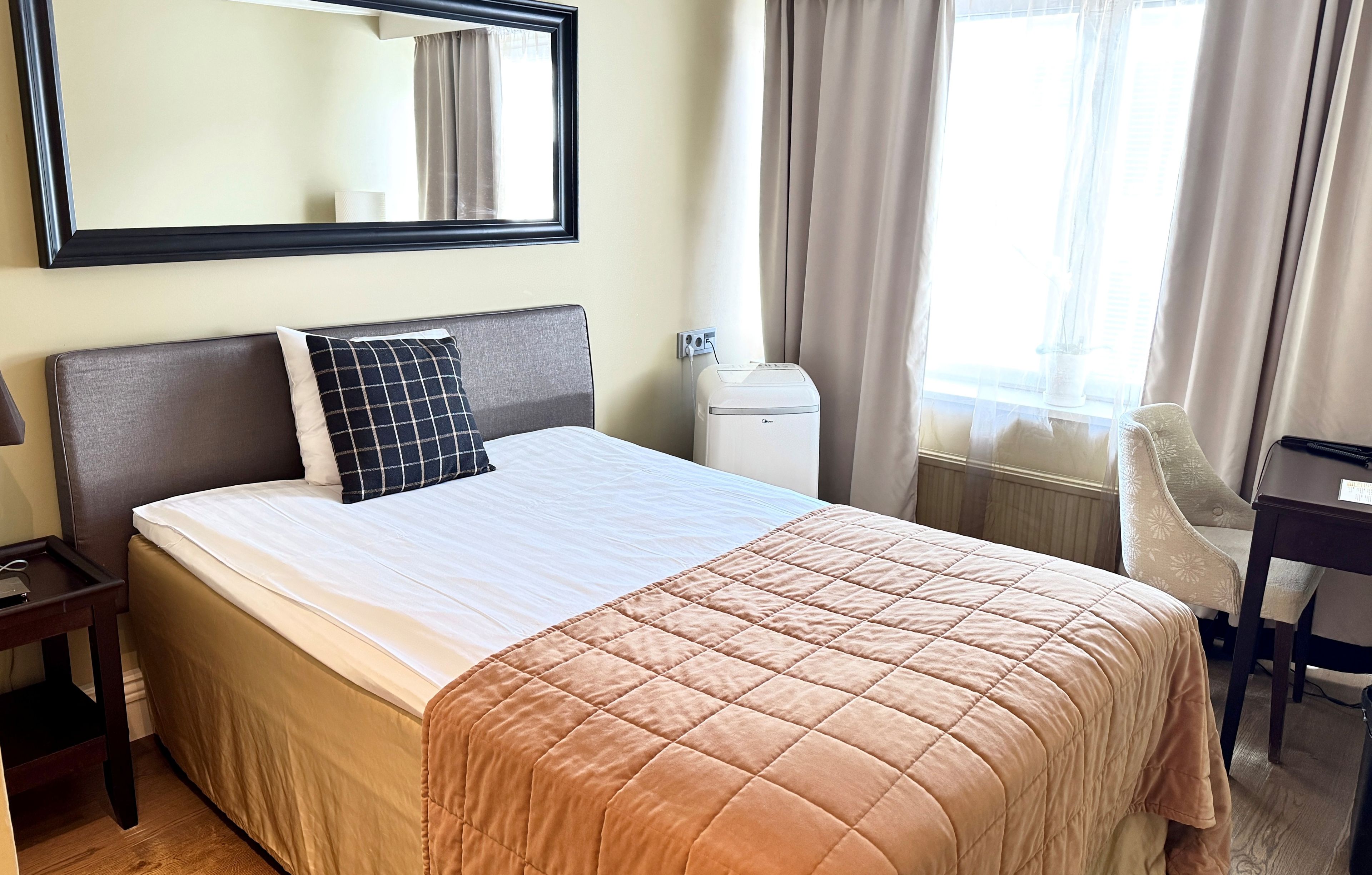 Ein Hotelzimmer mit Bett, Schreibtisch, Stuhl, Spiegel und einem Fenster mit Vorhängen.