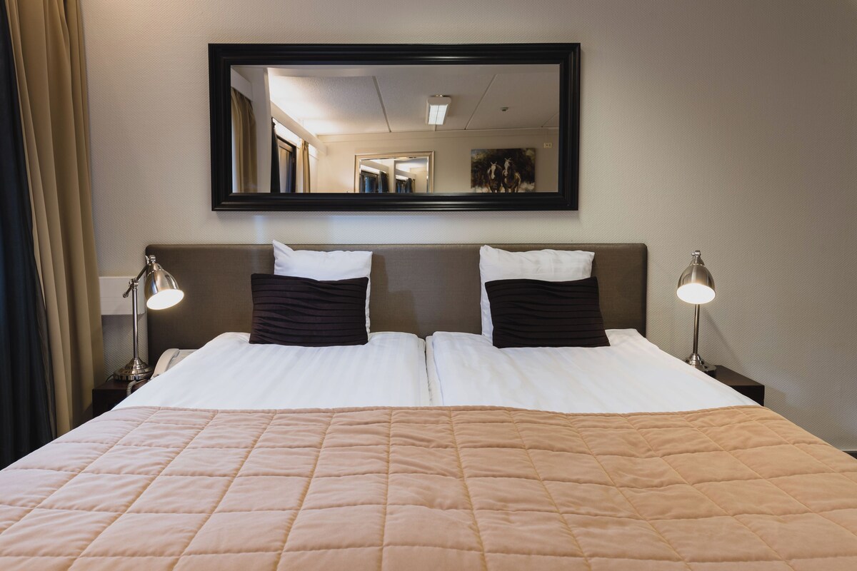 A hotel room with a large bed, two bedside lamps, a mirror above the bed, and a painting on the wall.
