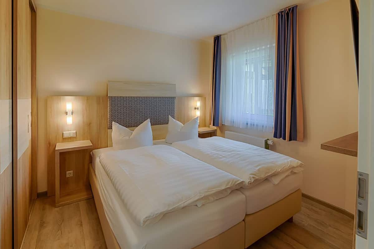 A double bed with two nightstands, a headboard with a light panel, and a window with curtains.