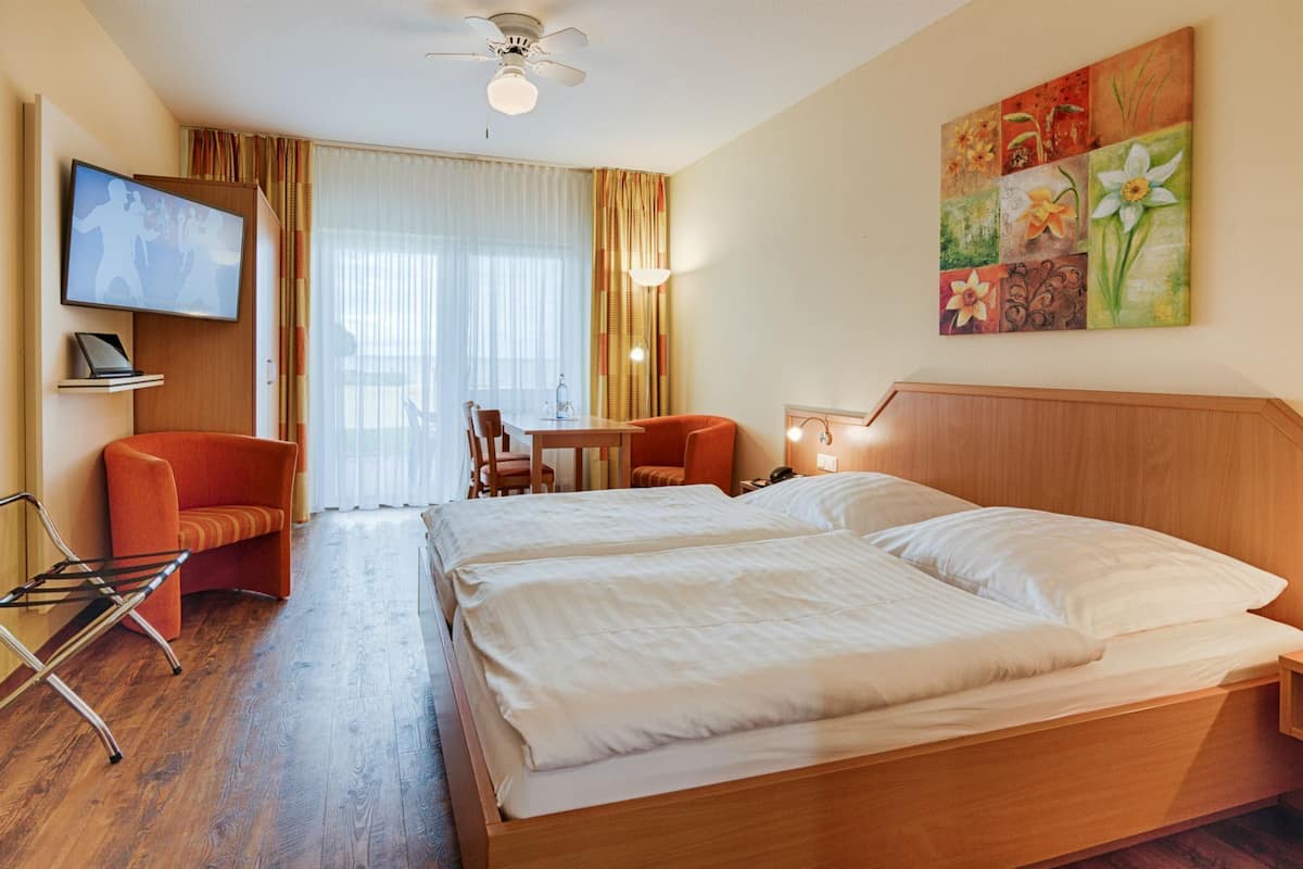 A hotel room with two beds, a desk, a chair, a TV, and a painting on the wall.