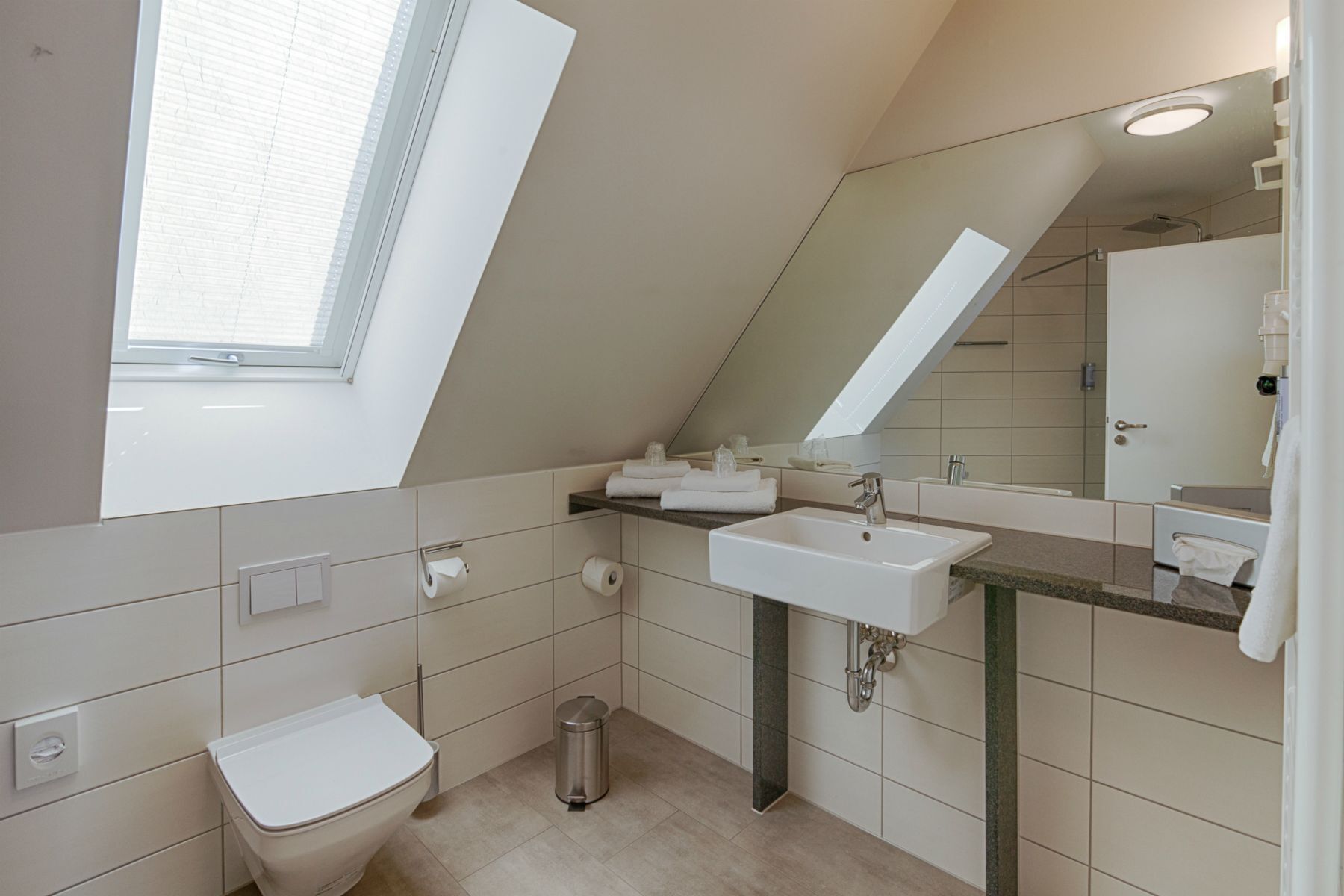 Et moderne badeværelse med ovenlys, toilet, vask og spejl.