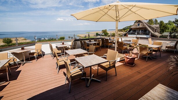 Un patio al aire libre con mesas y sillas, con vista a una playa y al océano.