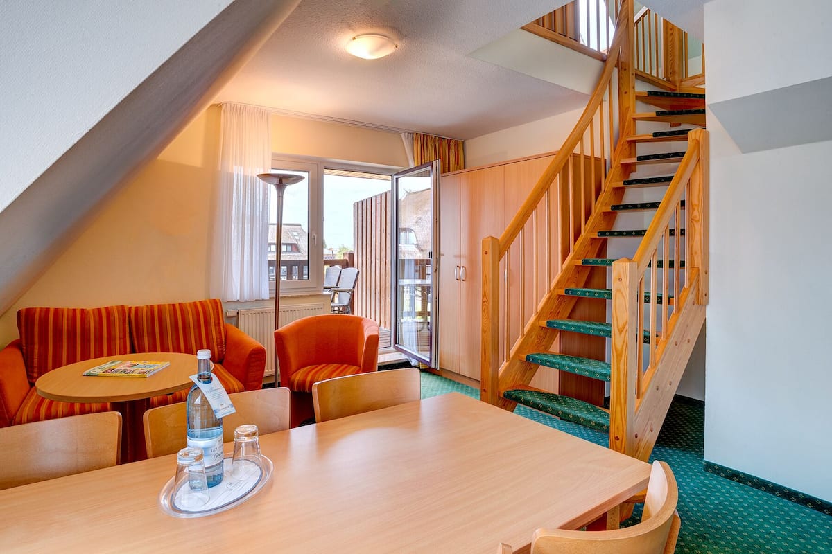 A cozy room with a wooden staircase, a dining table with chairs, and a view of the outside balcony.