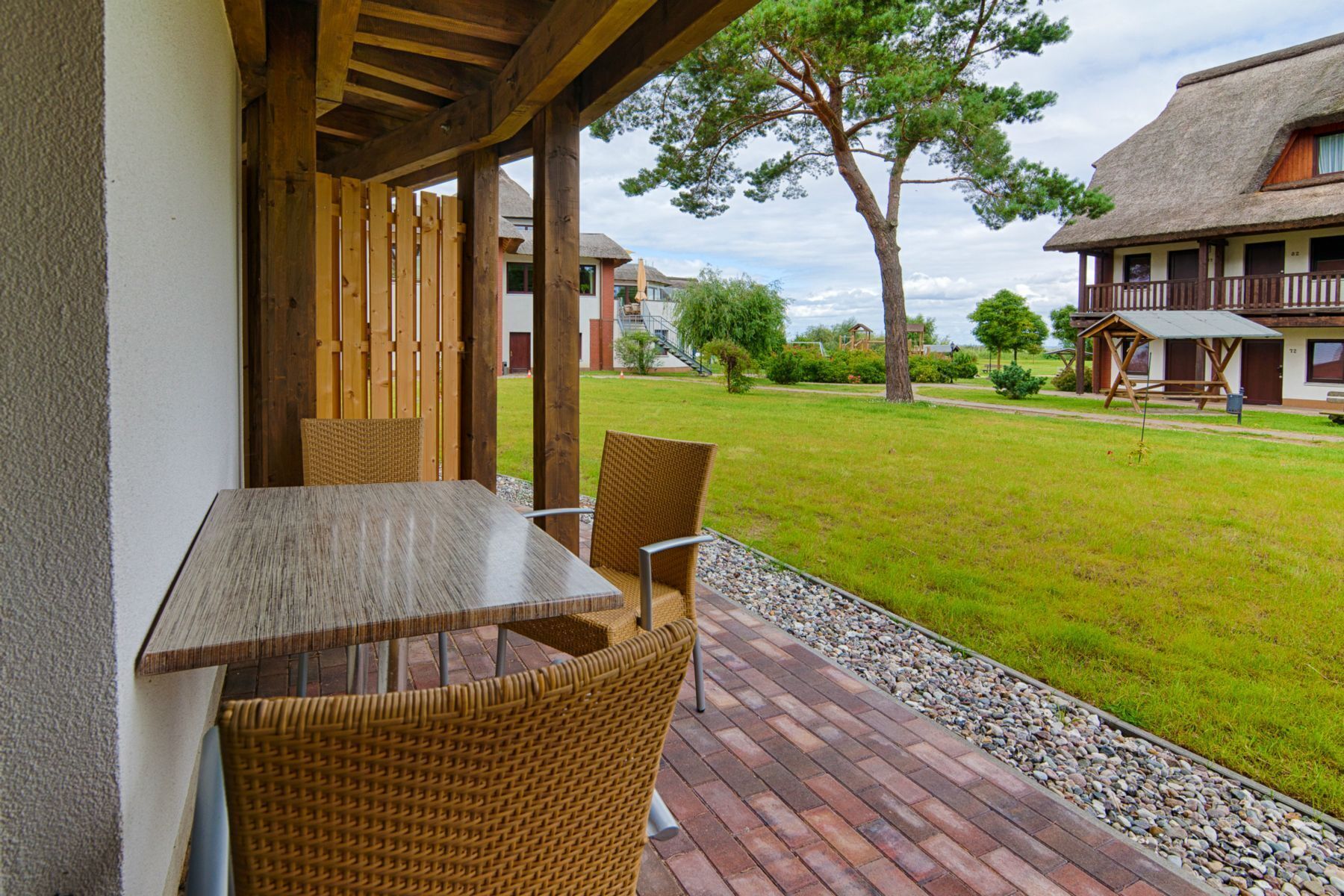 A patio with a table and chairs, a grassy lawn, and a building with a thatched roof in the background.