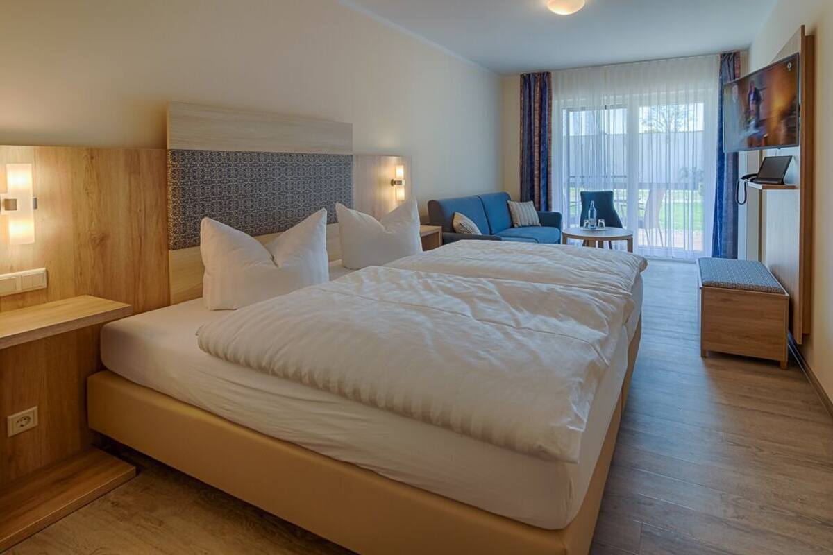 A hotel room with a large bed, a desk, a chair, a TV, and a view of the outdoors.