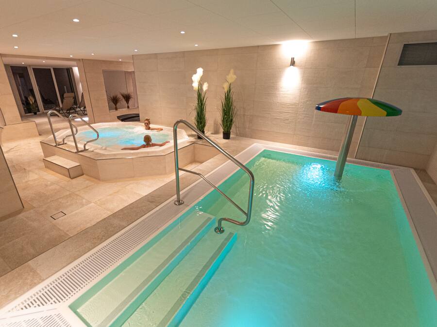 Una piscina con hidromasaje, una escalera y un paraguas colorido.