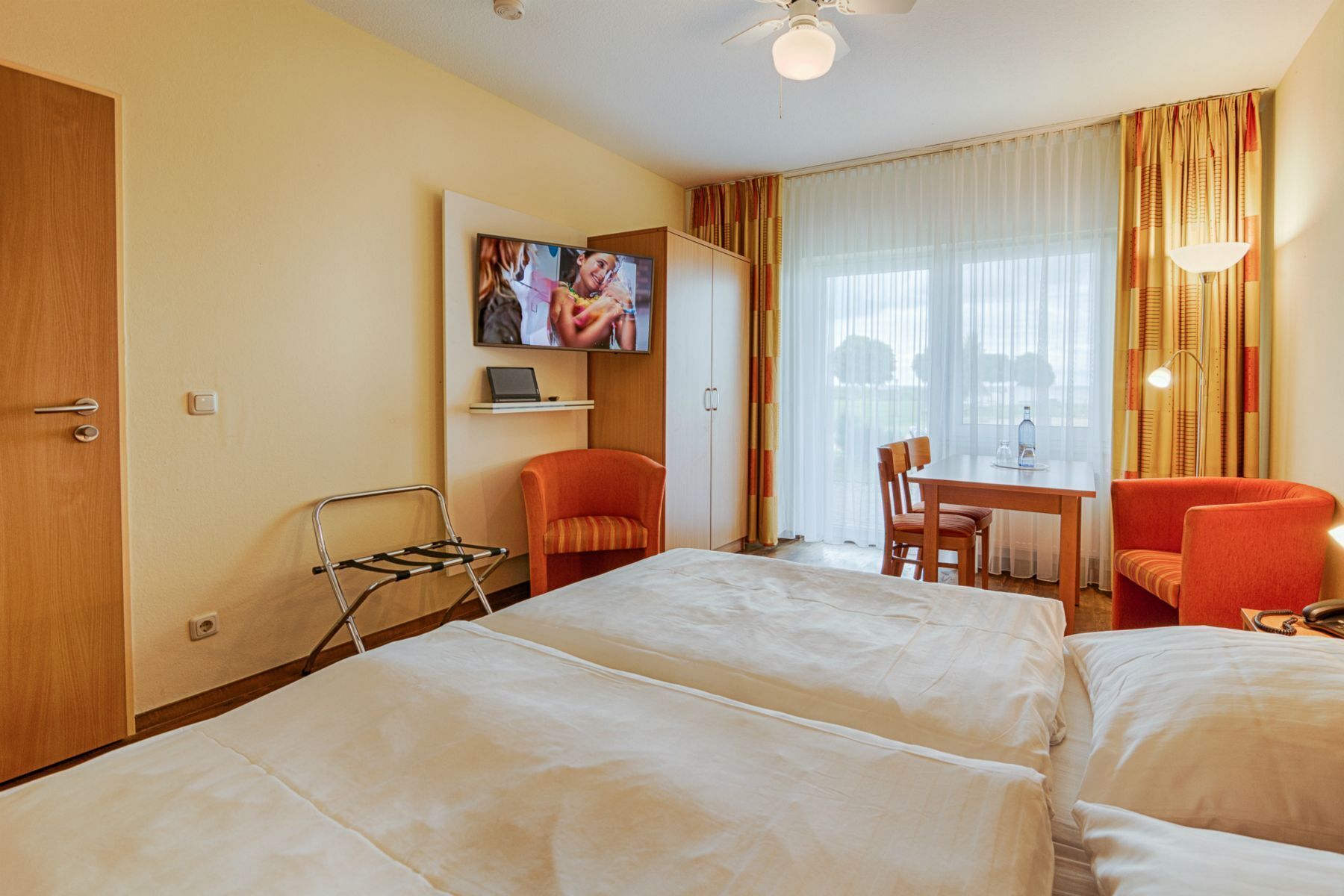 Een hotelkamer met twee bedden, een televisie, een bureau met stoel en een raam met gordijnen.