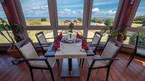 Mesa de comedor para seis personas con sillas, vista al mar y plantas en macetas.