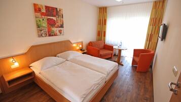 A hotel room with a wooden bed, a small table, an orange chair, and a painting on the wall.