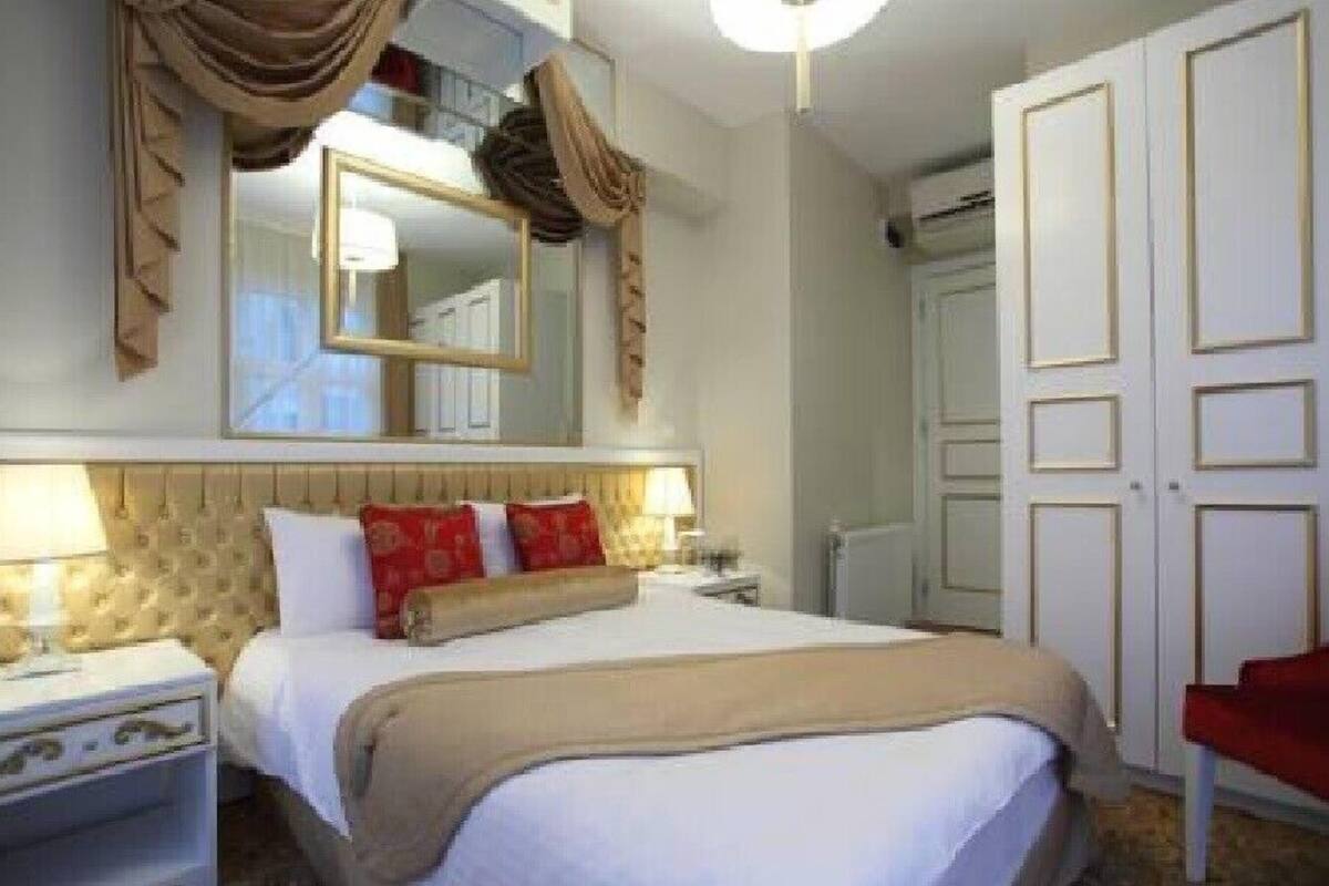 A hotel room with a large bed, a mirror above it, a wardrobe, and a red chair.