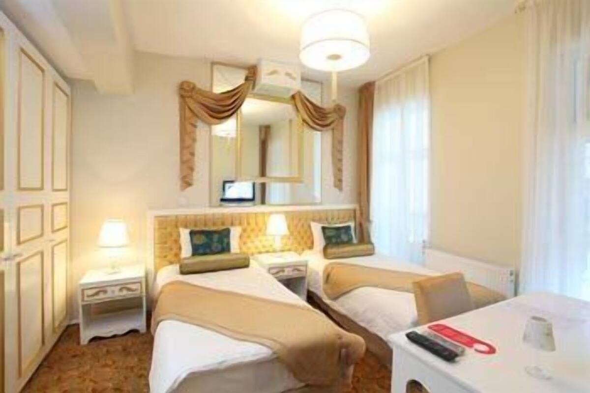 A hotel room with two beds, a desk, a lamp, a mirror, and a window with curtains.
