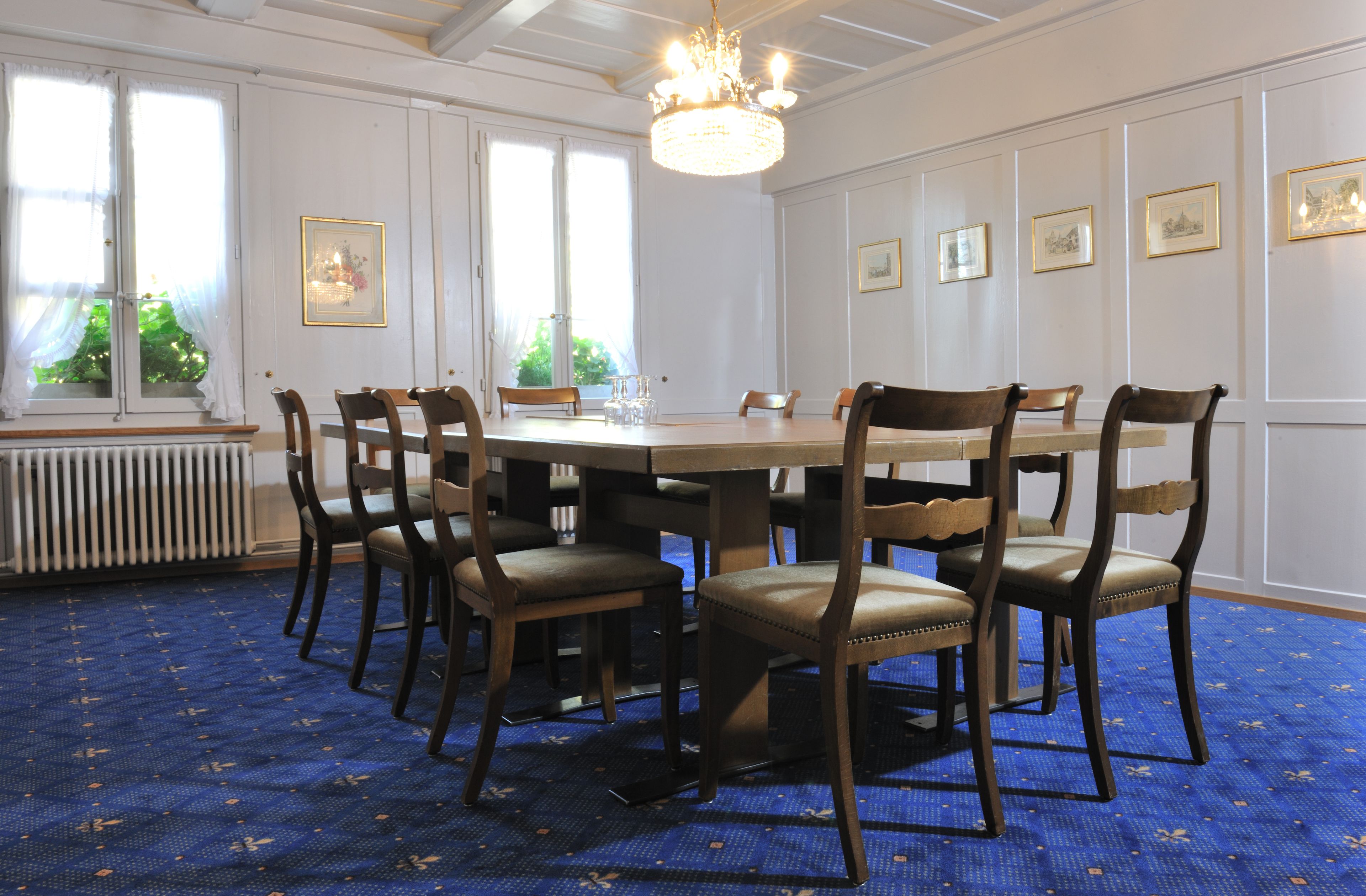Une salle à manger avec une grande table, six chaises, un lustre et des tableaux encadrés accrochés aux murs.