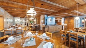 A spacious dining area with wooden tables and chairs, a kitchen in the background, and a high wooden ceiling. - SEELANDHOTEL Weisses Kreuz (Lyss)