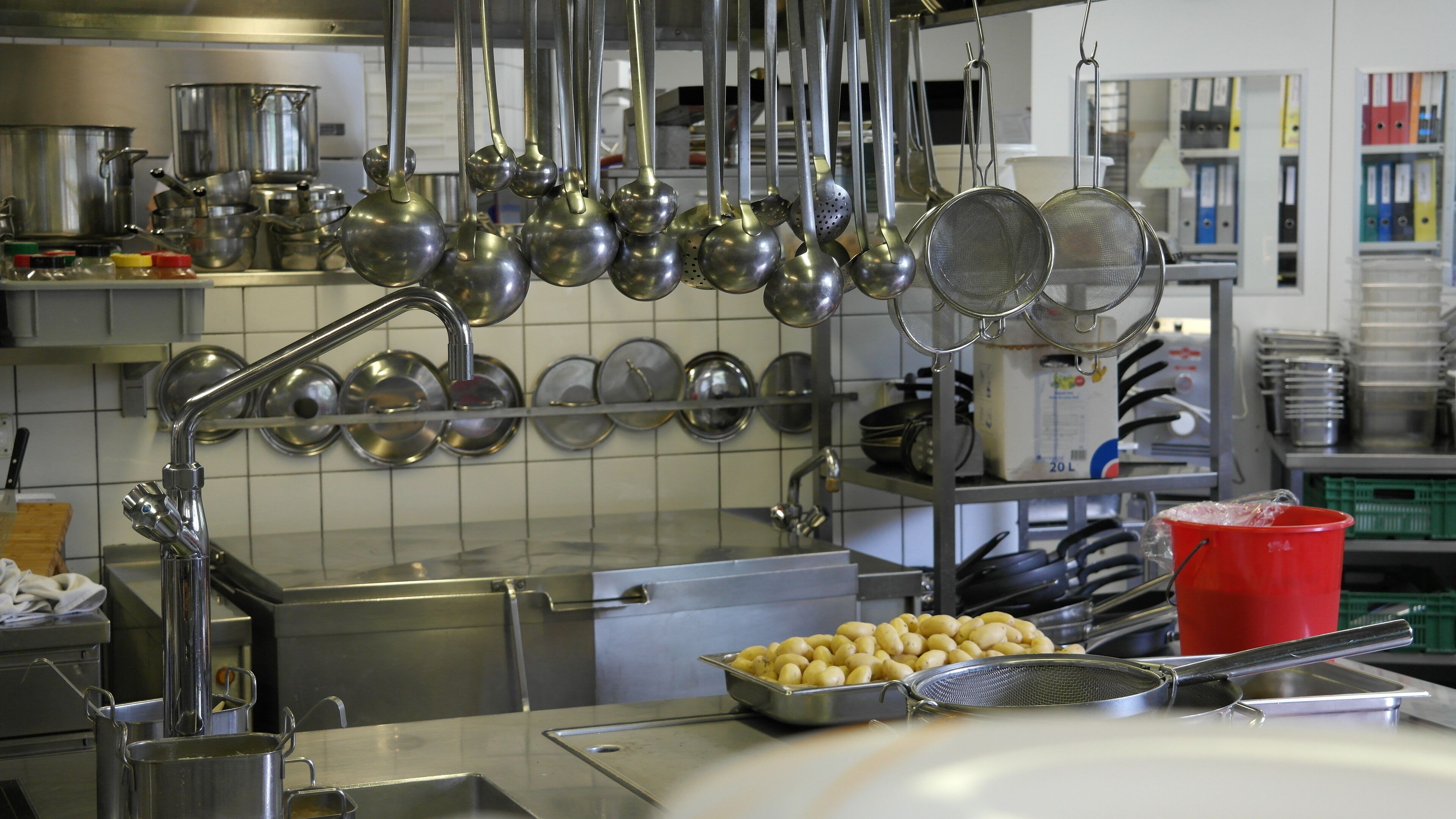 Une cuisine équipée d’appareils électroménagers en acier inoxydable, avec des ustensiles de cuisine suspendus au-dessus de l’évier et un seau rouge posé sur le plan de travail.
